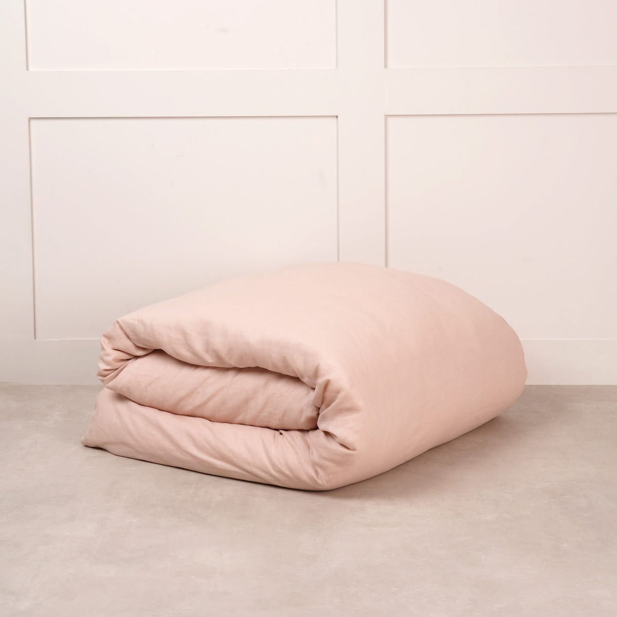 Cuddledown linen duvet cover in Blush, neatly folded on a stone floor against a white panelled wall