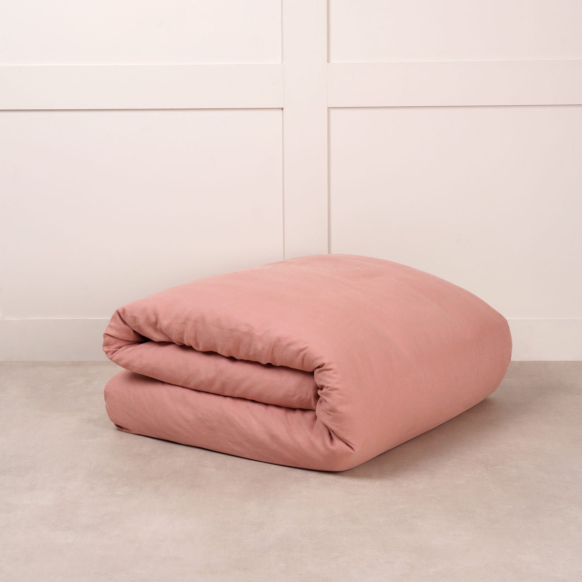 Cuddledown linen duvet cover in Canyon Pink, neatly folded on a stone floor against a white panelled wall