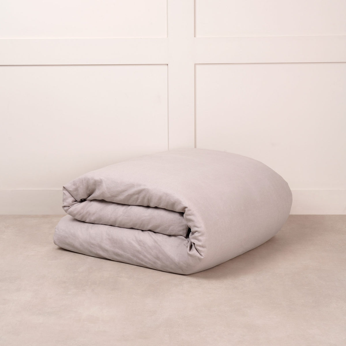Cuddledown linen duvet cover in Dove Grey, neatly folded on a stone floor against a white panelled wall