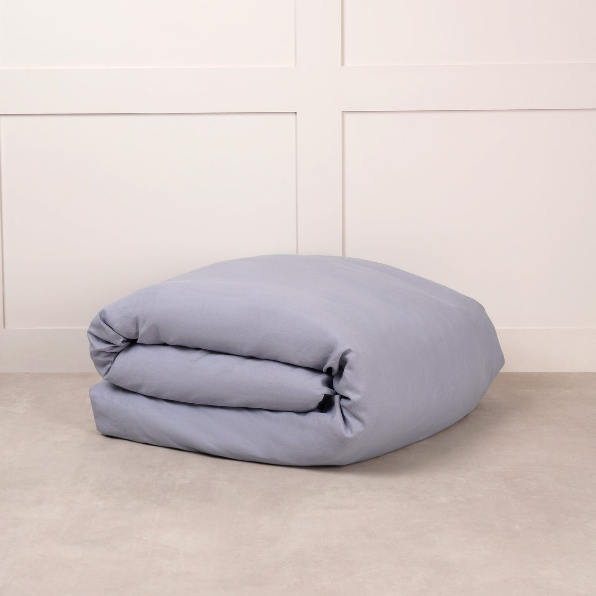 Cuddledown linen duvet cover in Lake Blue, neatly folded on a stone floor against a white panelled wall