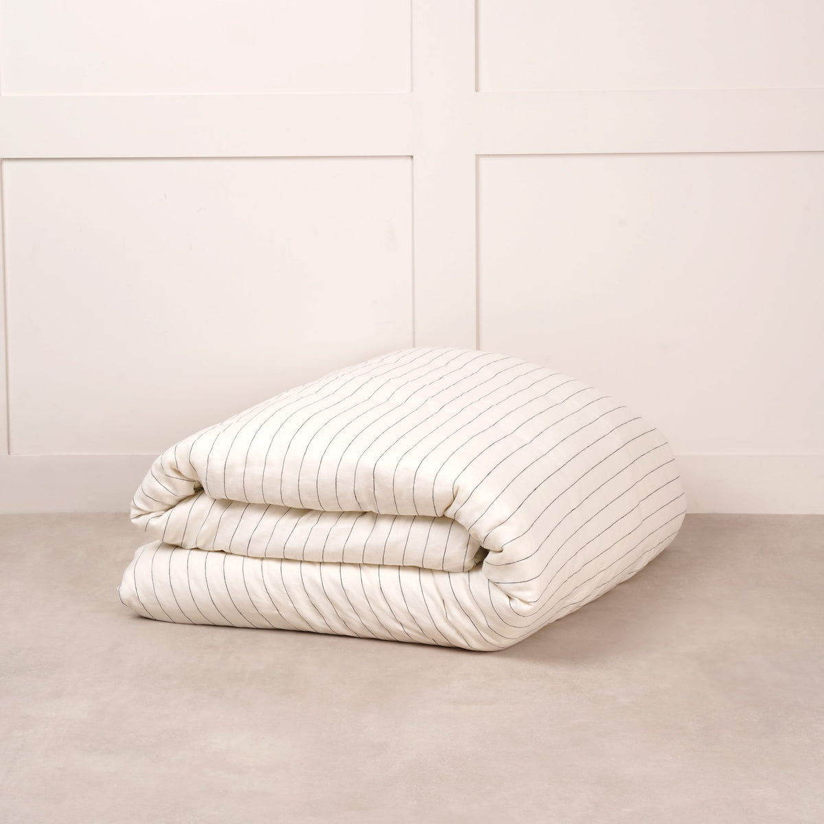 Cuddledown linen duvet cover in Luna Stripe, neatly folded on a stone floor against a white panelled wall