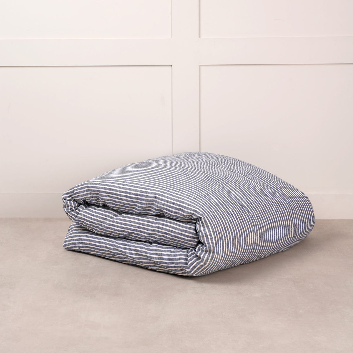 Cuddledown linen duvet cover in Midnight Stripe, neatly folded on a stone floor against a white panelled wall