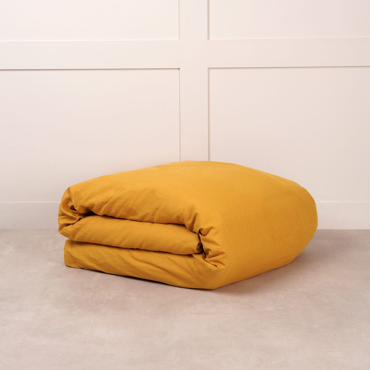 Cuddledown linen duvet cover in Mustard Yellow, neatly folded on a stone floor against a white panelled wall