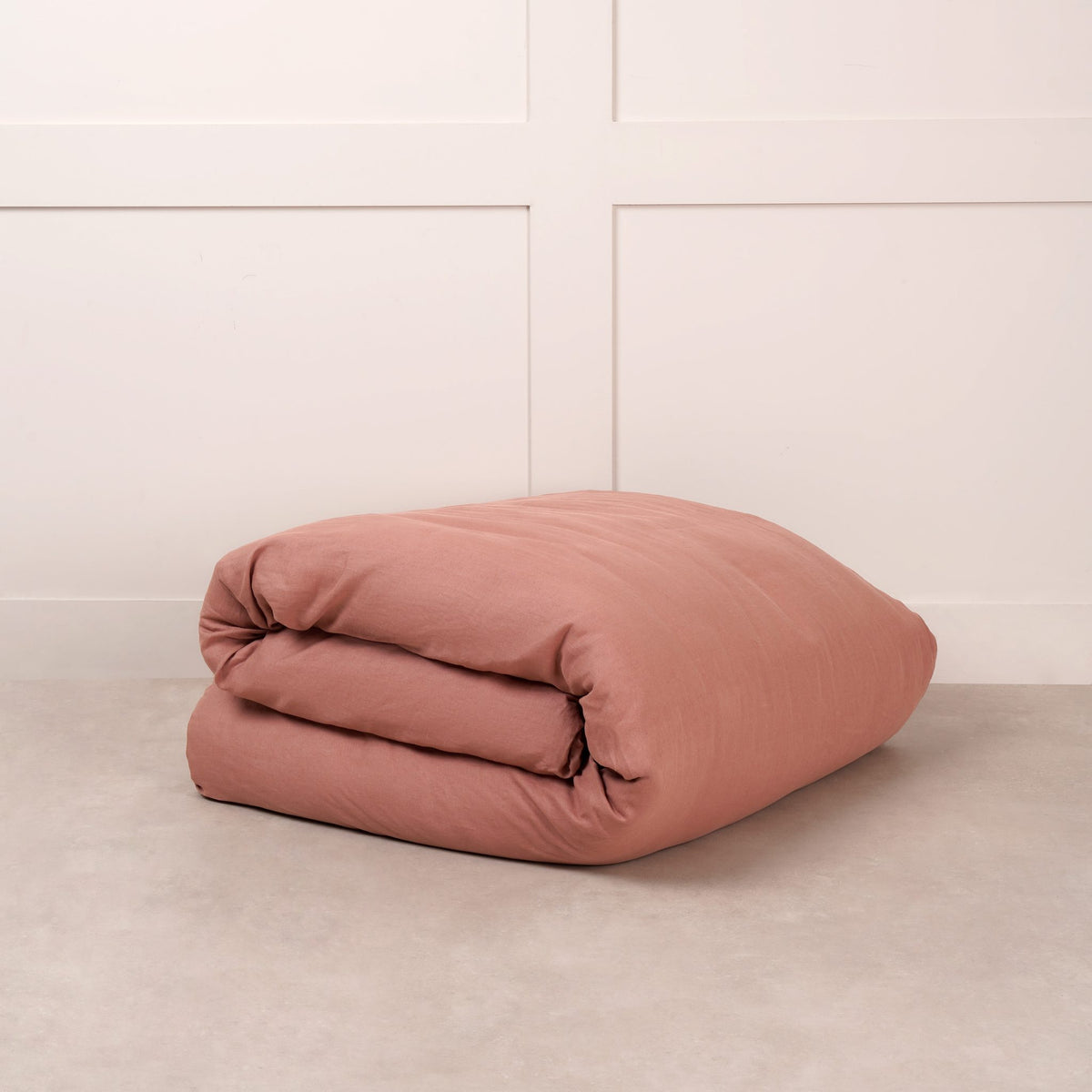 Cuddledown linen duvet cover in Rust, neatly folded on a stone floor against a white panelled wall