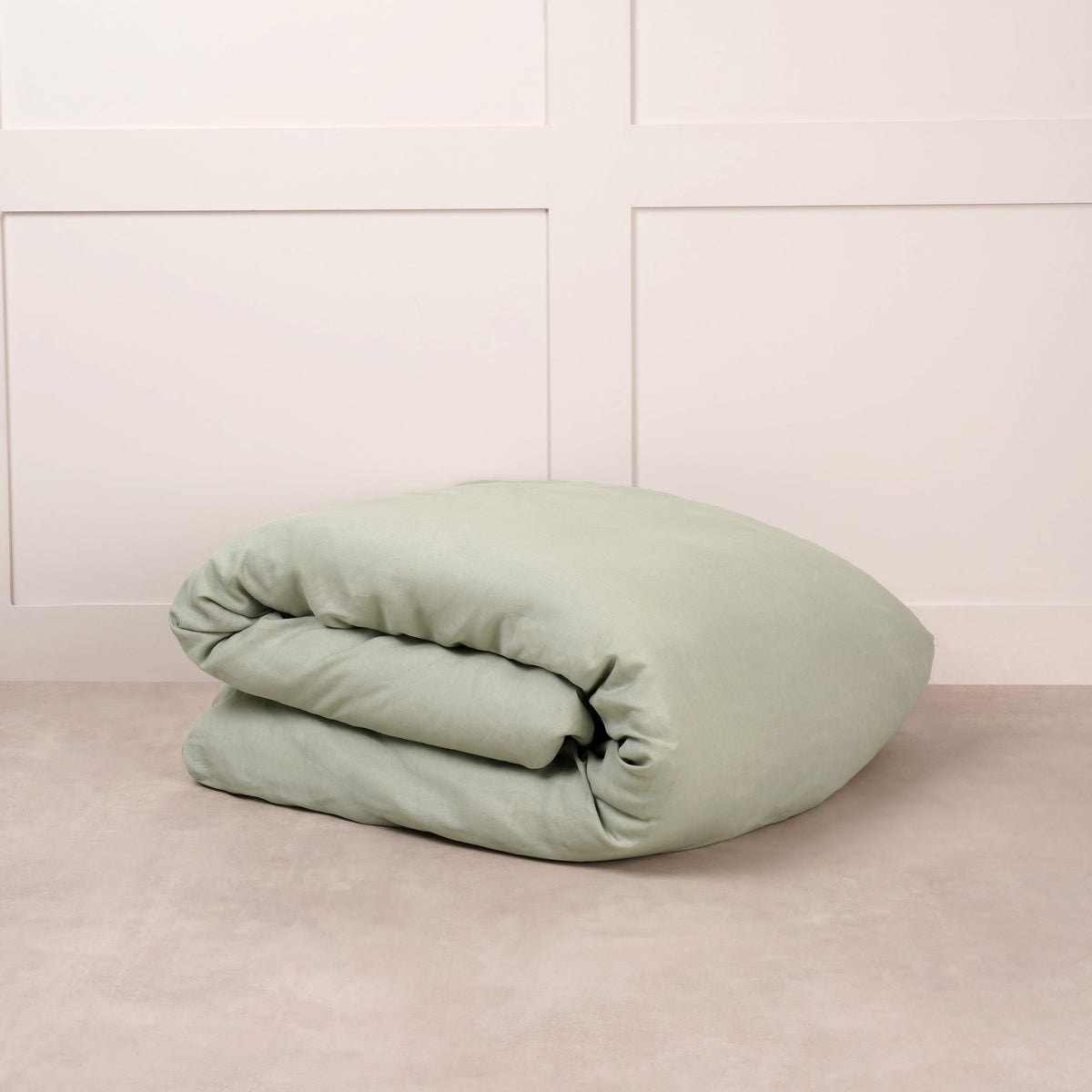 Cuddledown linen duvet cover in Sage Green, neatly folded on a stone floor against a white panelled wall