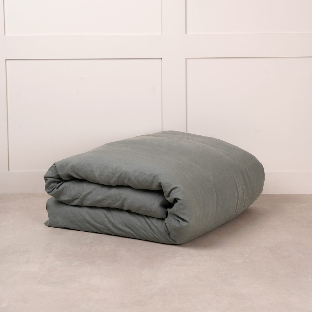Cuddledown linen duvet cover in Sea, neatly folded on a stone floor against a white panelled wall