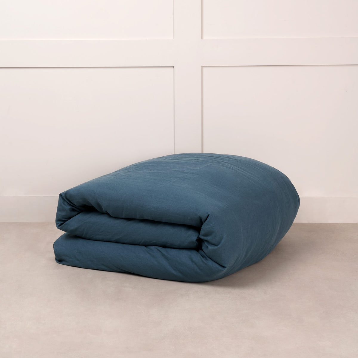 Cuddledown linen duvet cover in Teal, neatly folded on a stone floor against a white panelled wall