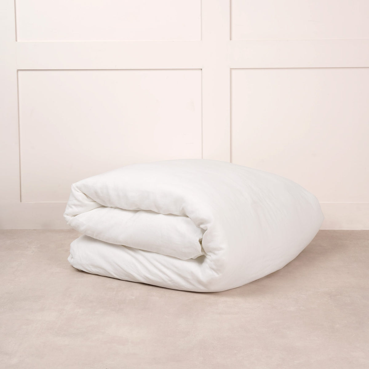 Cuddledown linen duvet cover in White, neatly folded on a stone floor against a white panelled wall