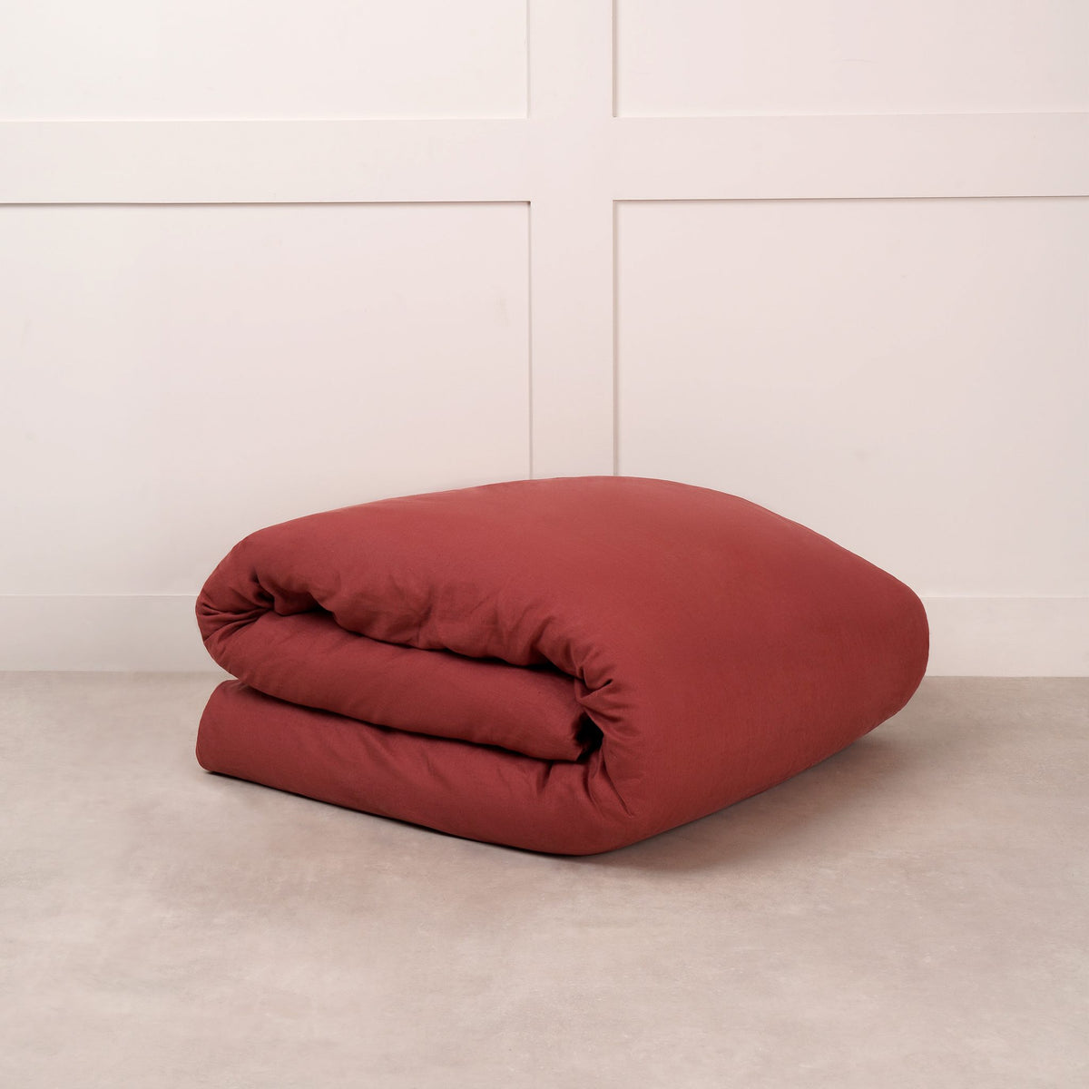 Cuddledown linen duvet cover in Wine, neatly folded on a stone floor against a white panelled wall