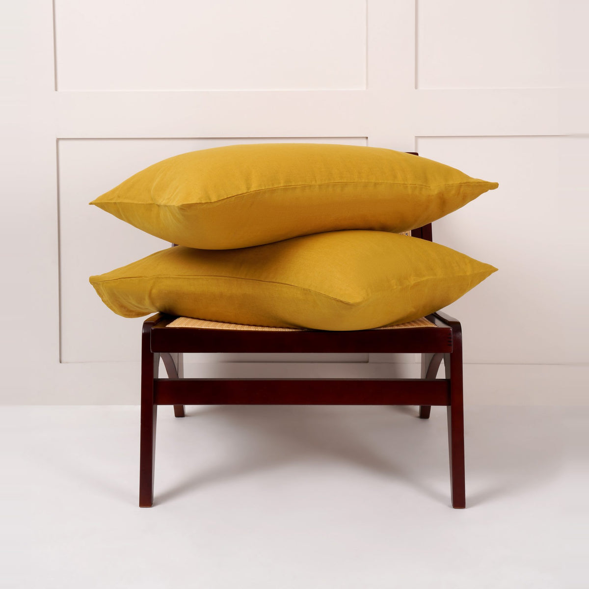 Cuddledown linen pillowcases in Ochre, pair of pillows stacked on a wooden chair against a white panelled wall